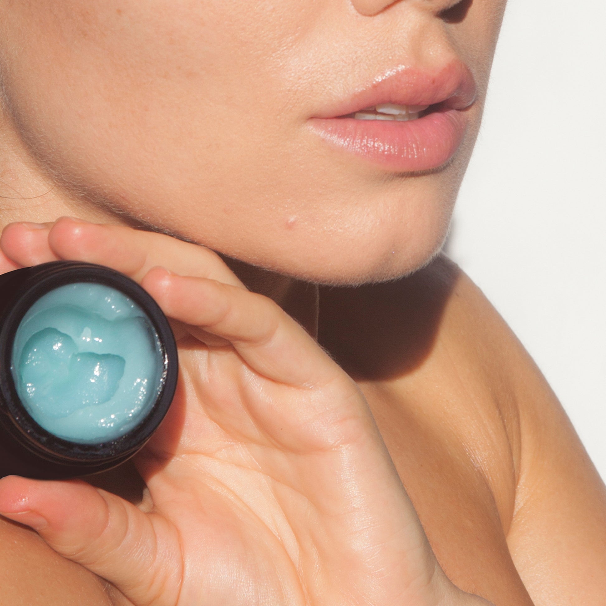 Person holding a small container of le blue balm near their face