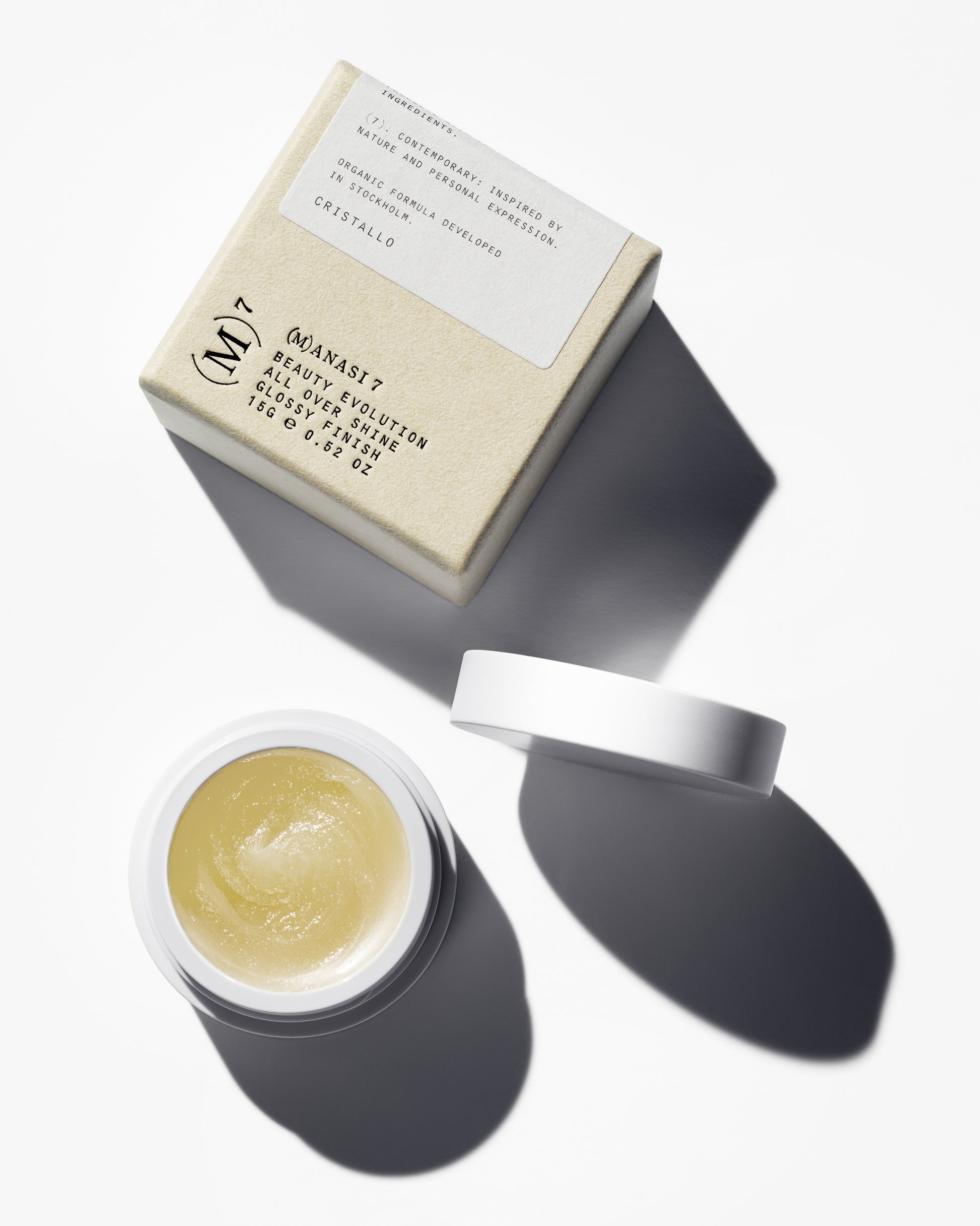 The Manasi 7 All over shine in the shade Cristallo in a small round container and its packaging on a white background