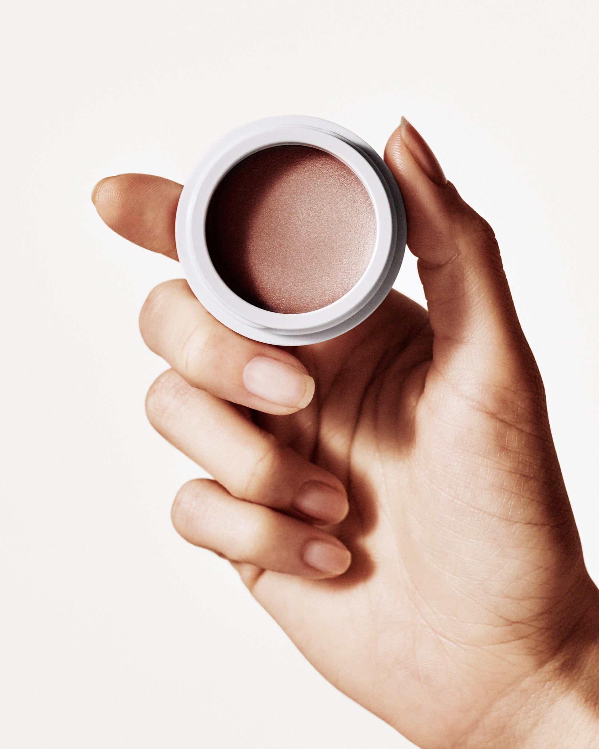 a hand holding the Manasi 7 Bronzelighter in the shade roseate in a small round container 