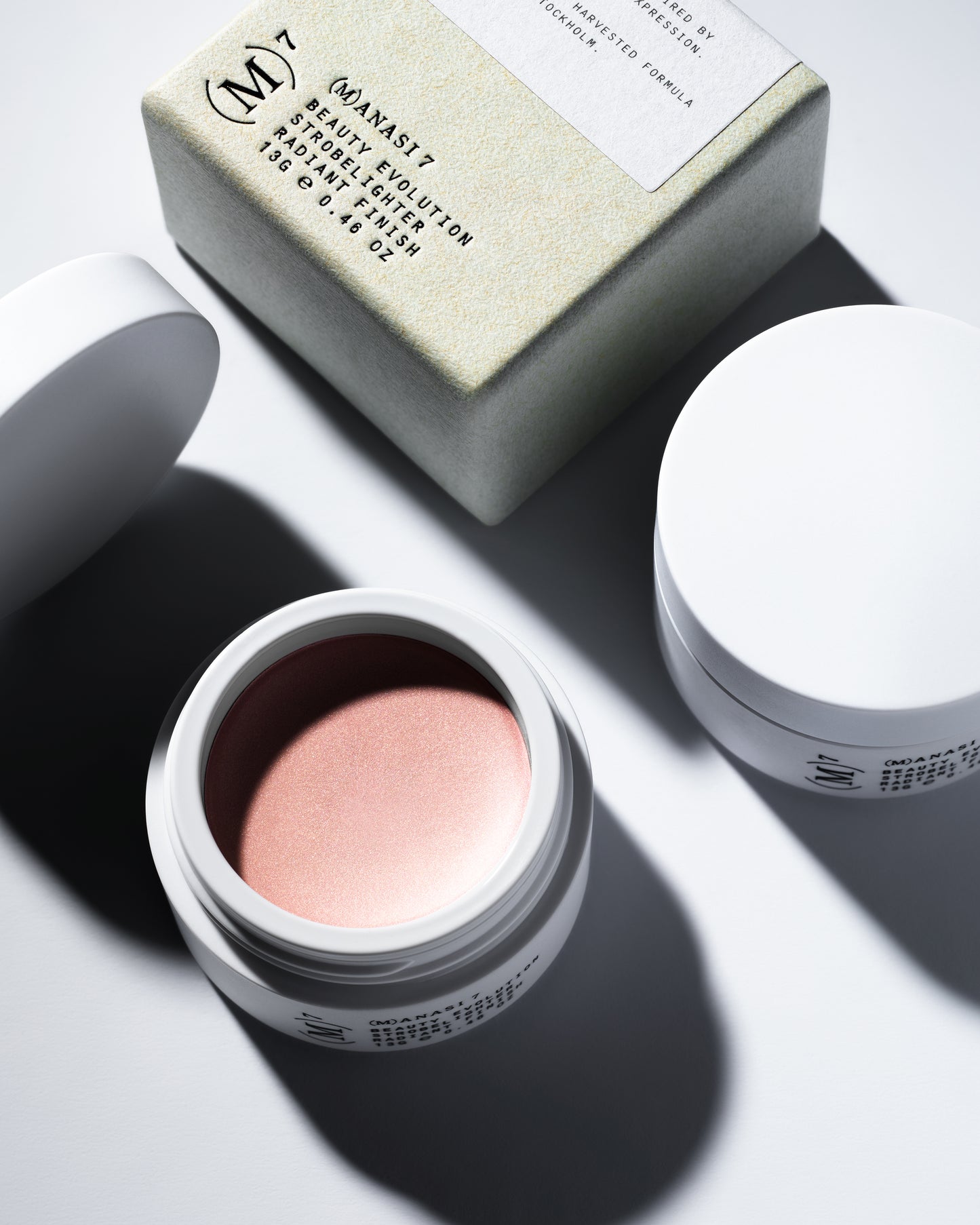 The Manasi 7 Strobelighter in the shade Sunrise in a small round container and its packaging on a white background