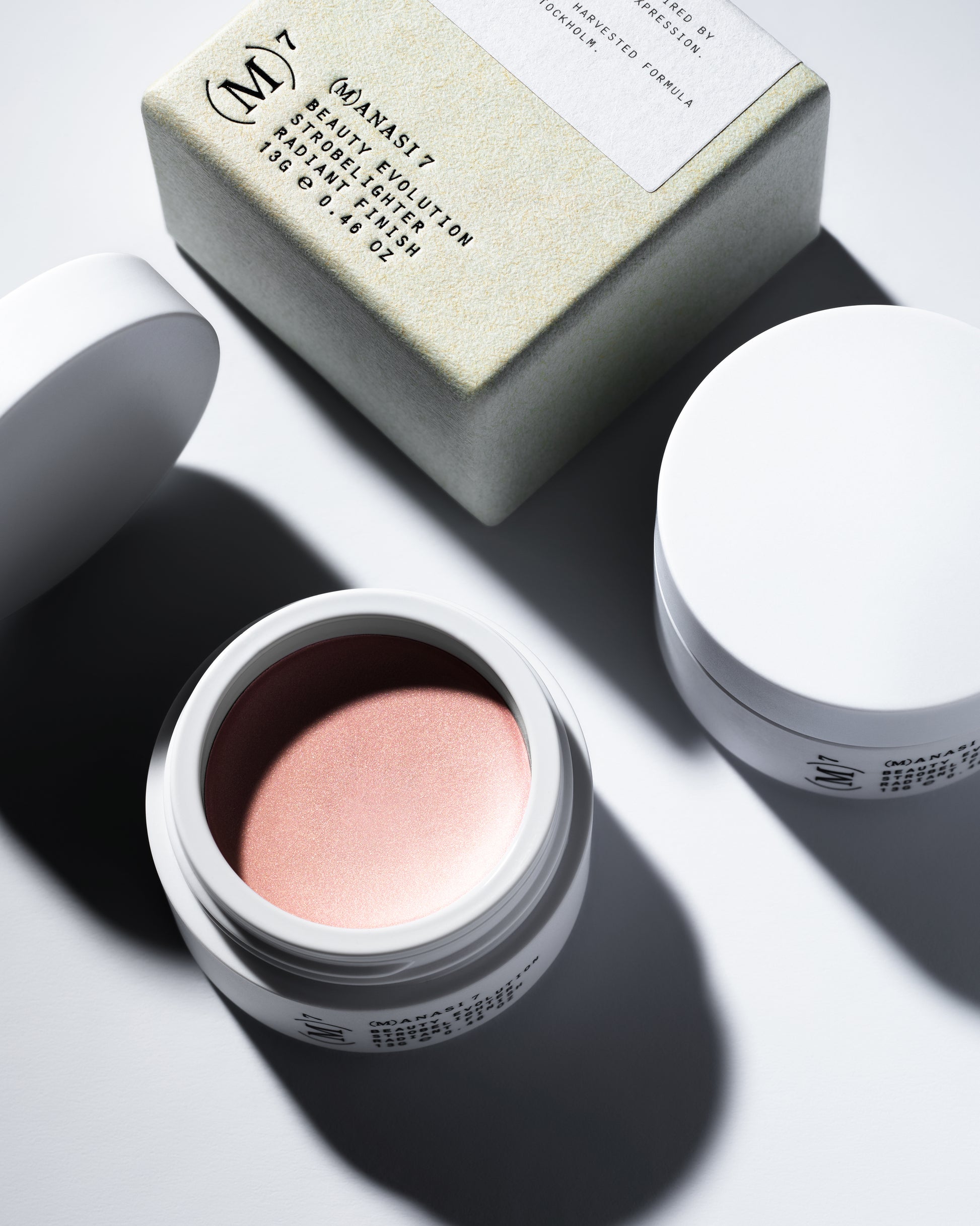 The Manasi 7 Strobelighter in the shade Sunrise in a small round container and its packaging on a white background