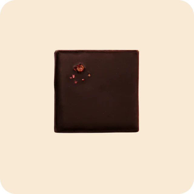 Square piece of dark chocolate with a few chocolate pieces on a beige background