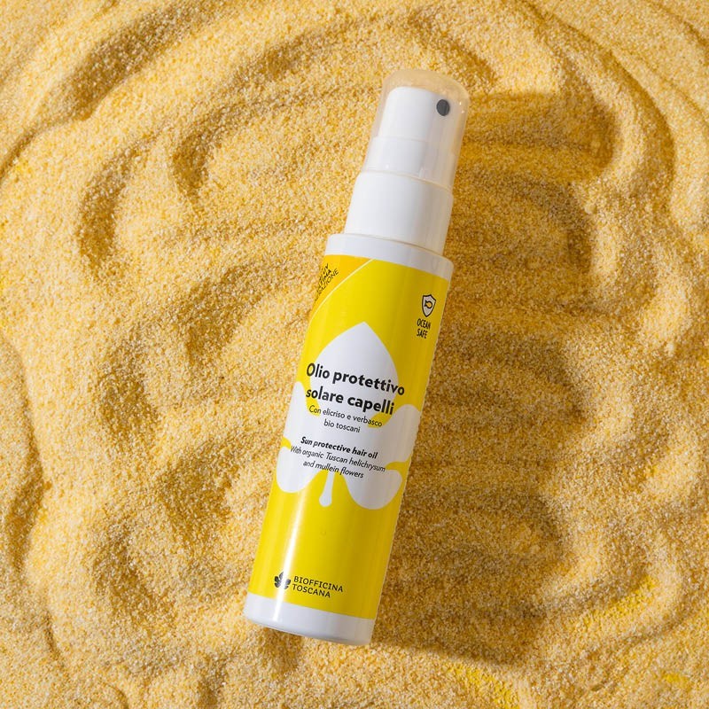 Yellow spray bottle of the sun protective hair oil by biofficina toscana with white cap on a sandy background