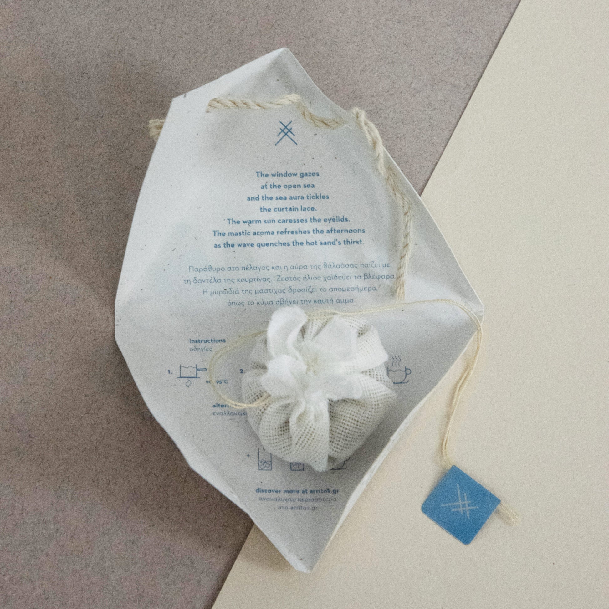 White cotton teabag on its packaging with text, next to a rock on a textured surface