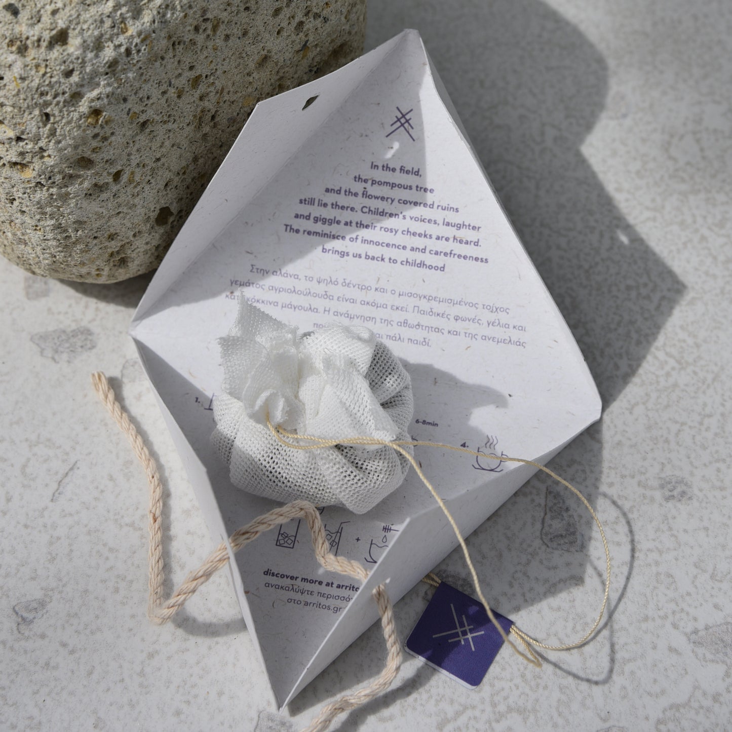 White cotton teabag on its packaging with text, next to a rock on a textured surface